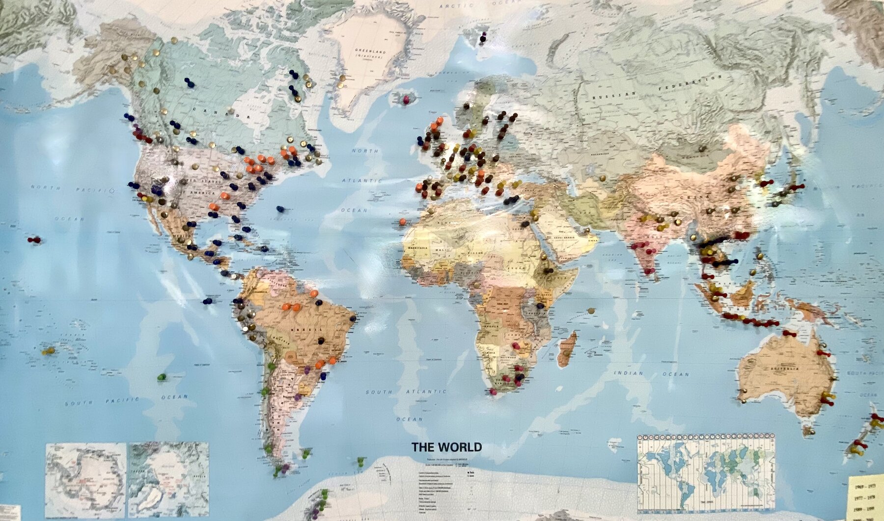 World map on the wall studded with colourful pins marking decades of travel
