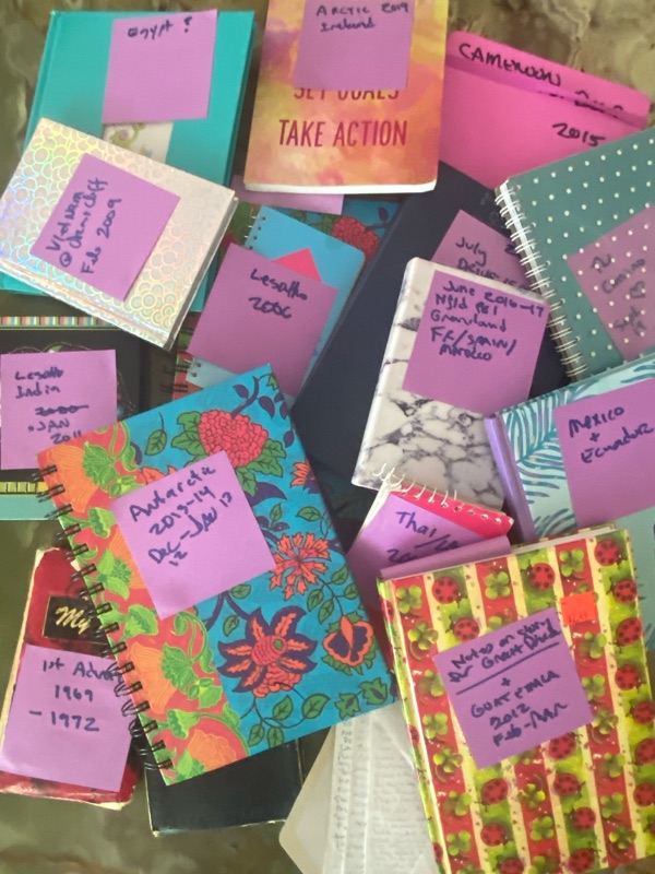 A pile of colourful travel journals labelled by hand with destinations and years, including Vietnam, Lesotho, Antarctica, Thailand, Mexico and Ecuador